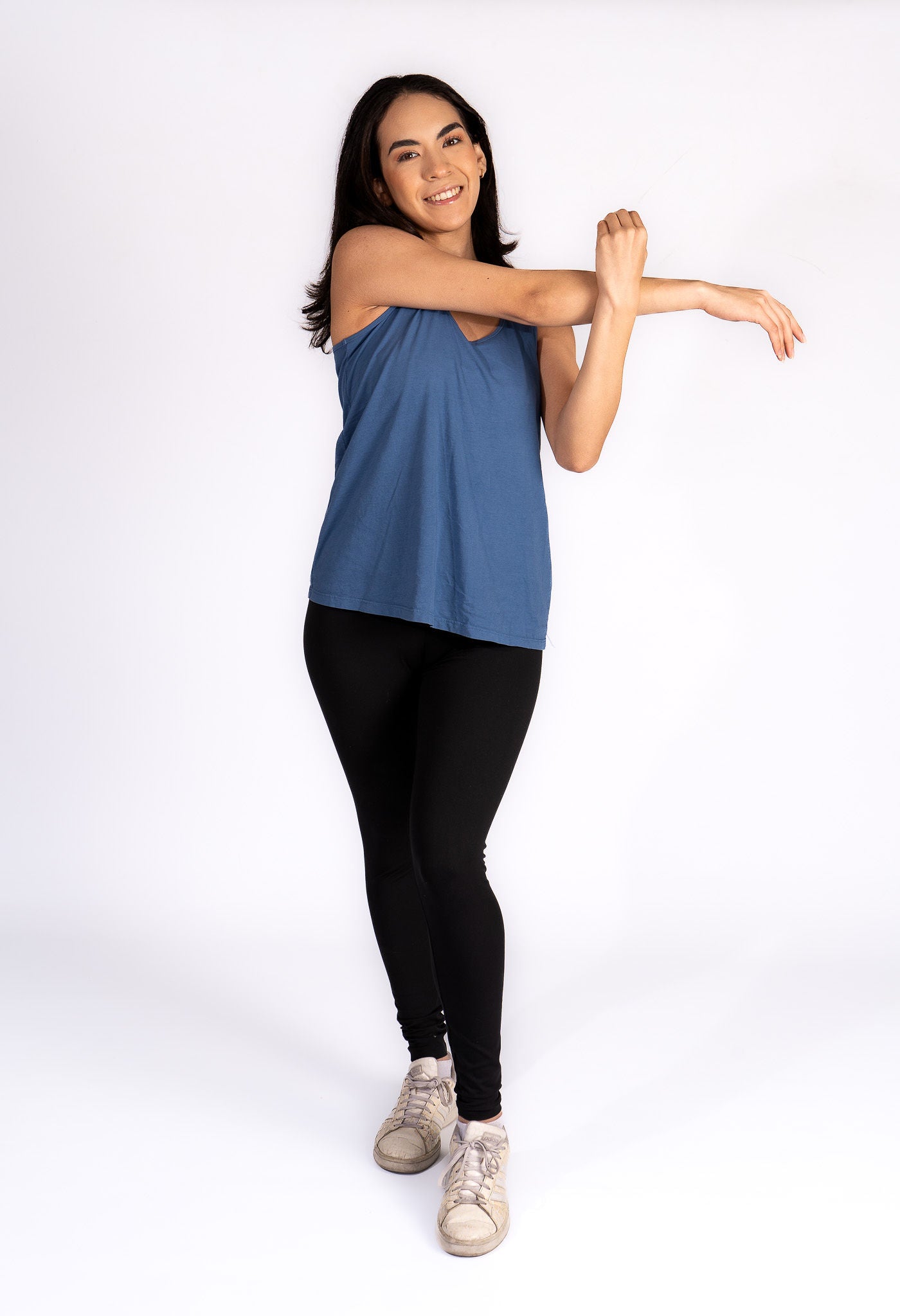 A woman wearing a purple flowy tank top with a scoop neckline and a round bottom hem, paired with a blue denim skirt.