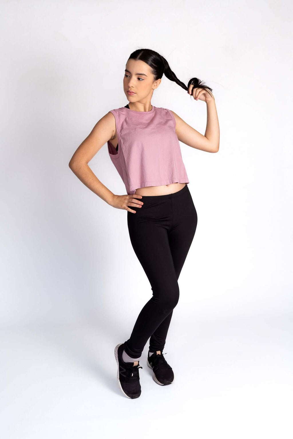 Woman wearing a pink sleeveless top and black leggings on a white background