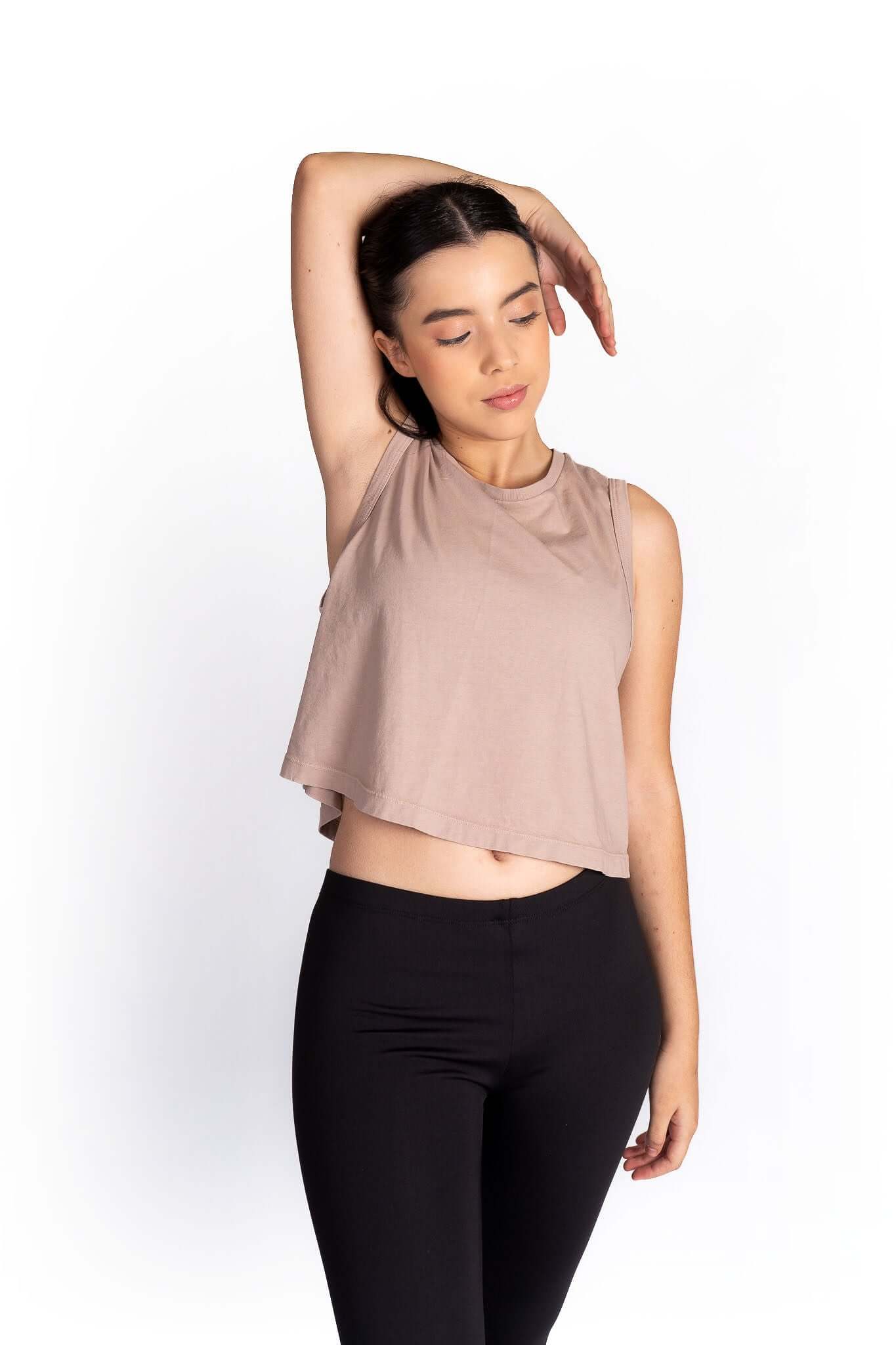 Woman wearing a beige sleeveless top and black pants on a white background