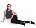 Woman sitting on a white background wearing a blue sleeveless top and black leggings.