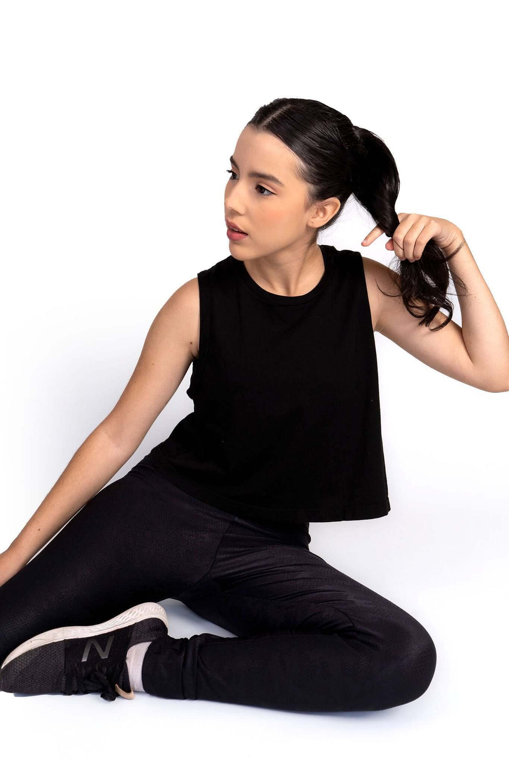 Woman wearing a black sleeveless top and pants sitting on a white background